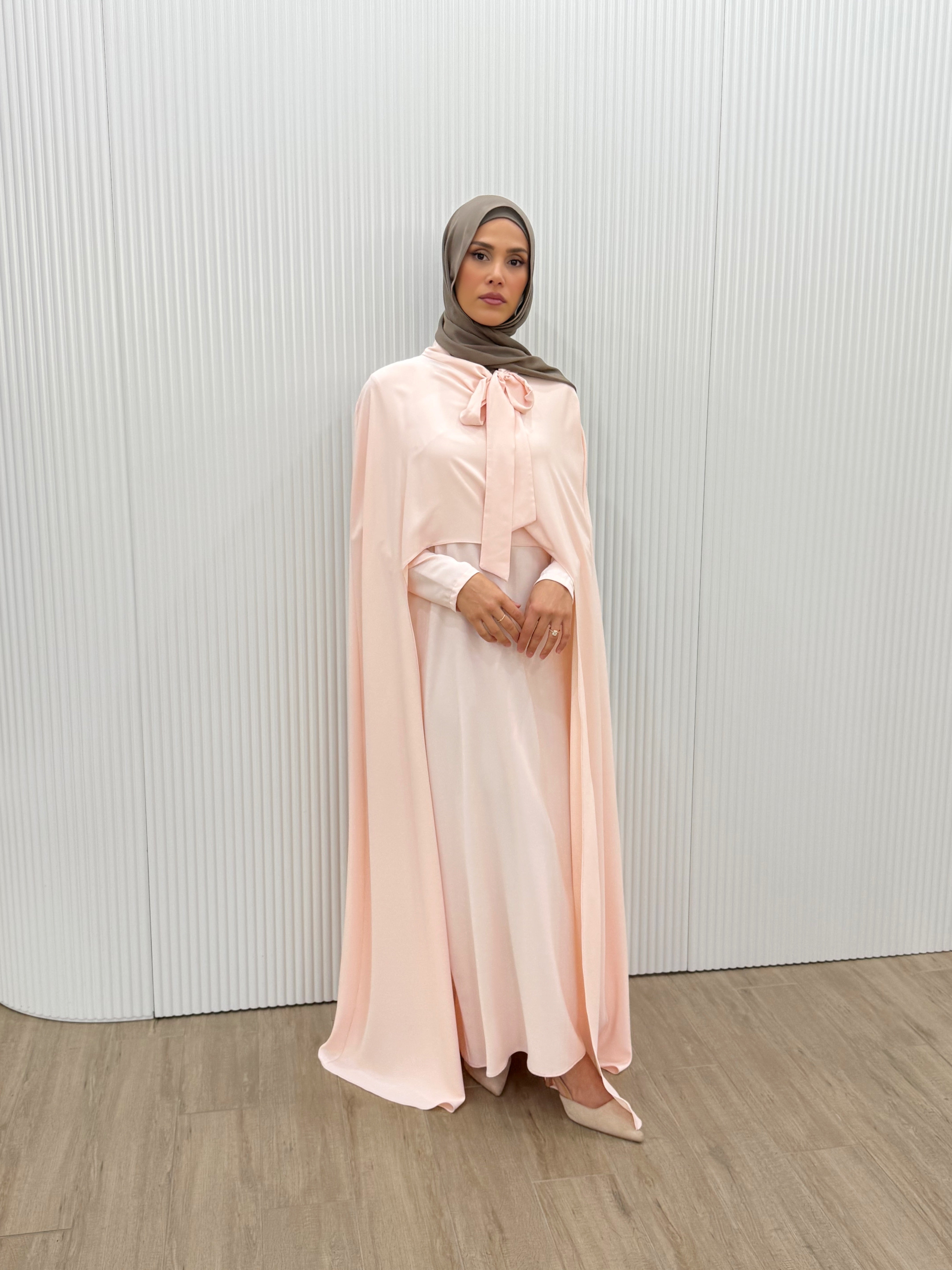 Grace meets fluidity in this captivating cape dress. Designed with a soft bow-tie neckline and a flowing overlay that drapes effortlessly over the shoulders, this piece radiates femininity and poise. These soft colours complement all skin tones, while the lightweight satin finish brings an understated elegance perfect for formal evenings and events.