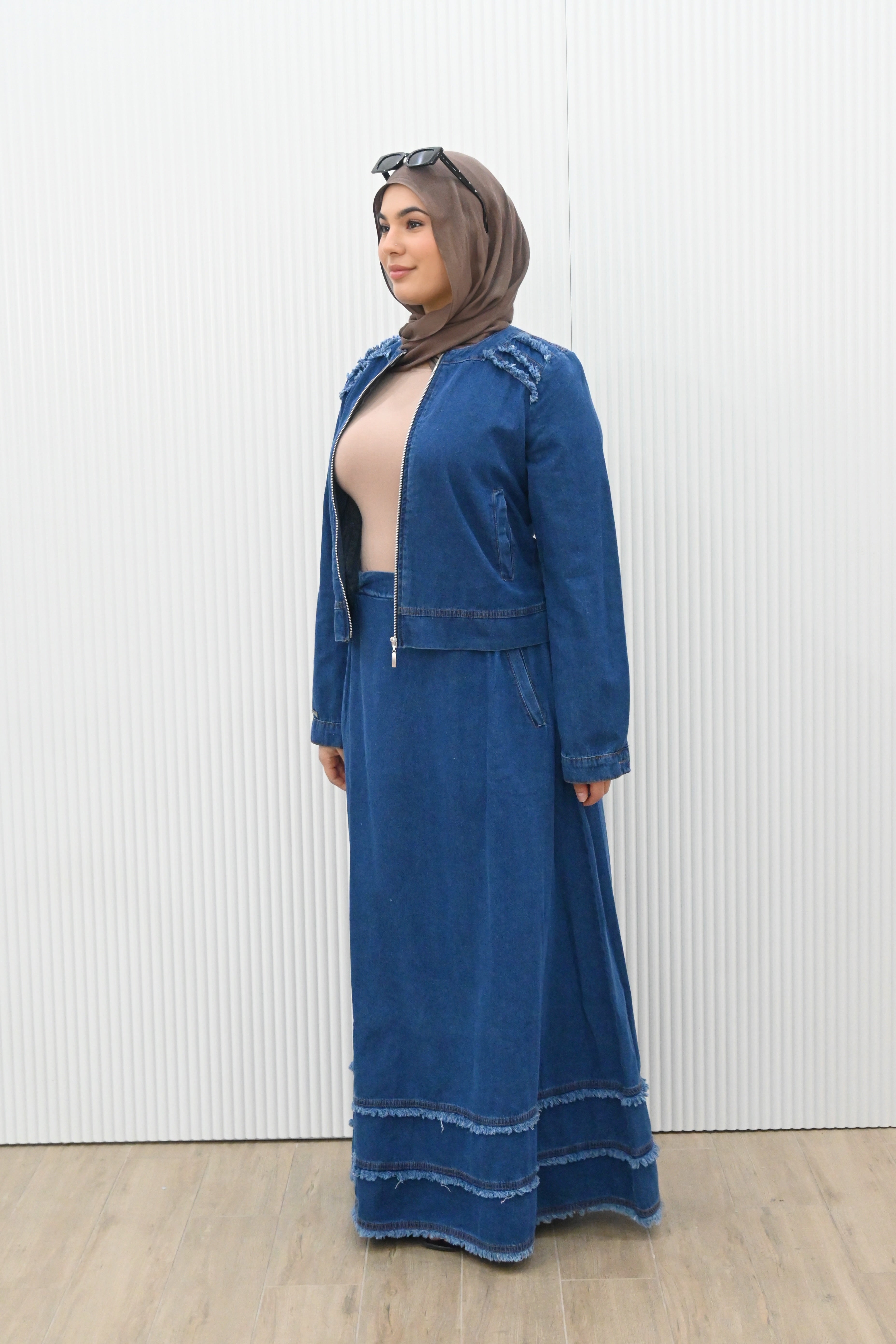 This is a two-piece modest denim-style outfit featuring a long A-line skirt and a matching zip-up jacket. The skirt has layered frayed hem details for a casual chic look, while the jacket is designed with full sleeves and light embroidery accents on the shoulder. Paired with a plain inner top, this set combines comfort and style, making it perfect for everyday wear or casual outings.