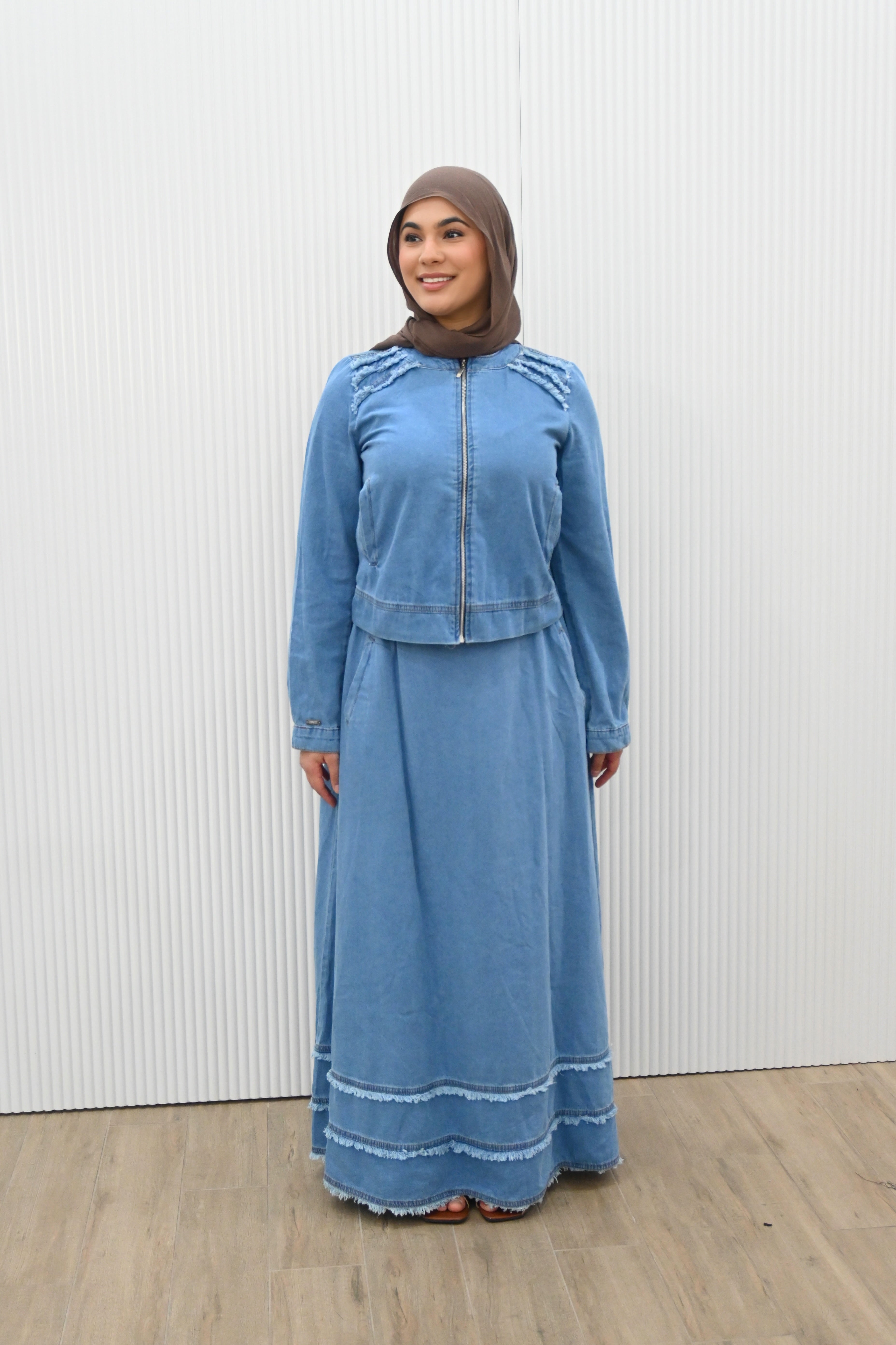 This is a two-piece modest denim-style outfit featuring a long A-line skirt and a matching zip-up jacket. The skirt has layered frayed hem details for a casual chic look, while the jacket is designed with full sleeves and light embroidery accents on the shoulder. Paired with a plain inner top, this set combines comfort and style, making it perfect for everyday wear or casual outings.