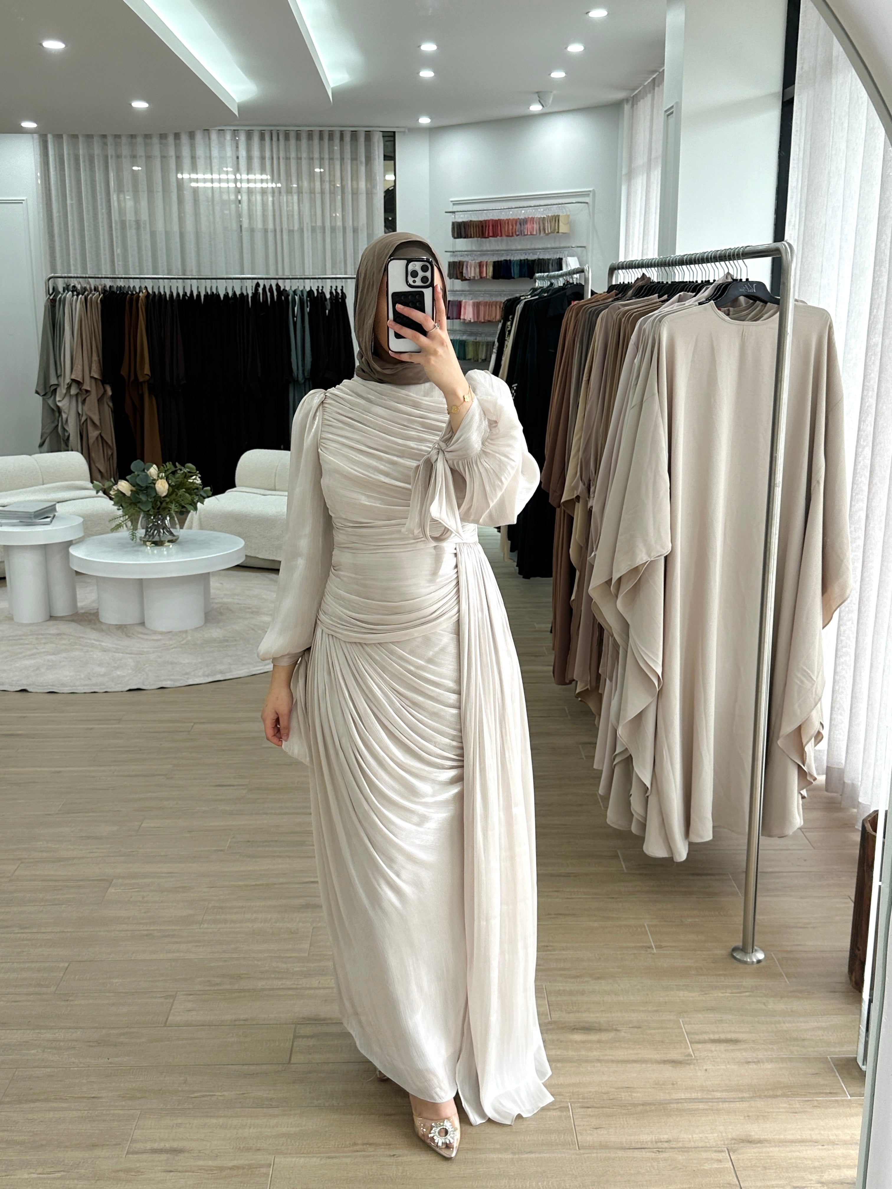 Model wearing the LAYAN Formal Dress, a floor-length gown in shiny organza fabric featuring all-over ruching, statement balloon sleeves with ribbon tie cuffs, a fitted waist with a drop panel, and a cascading skirt for an elegant, formal look.