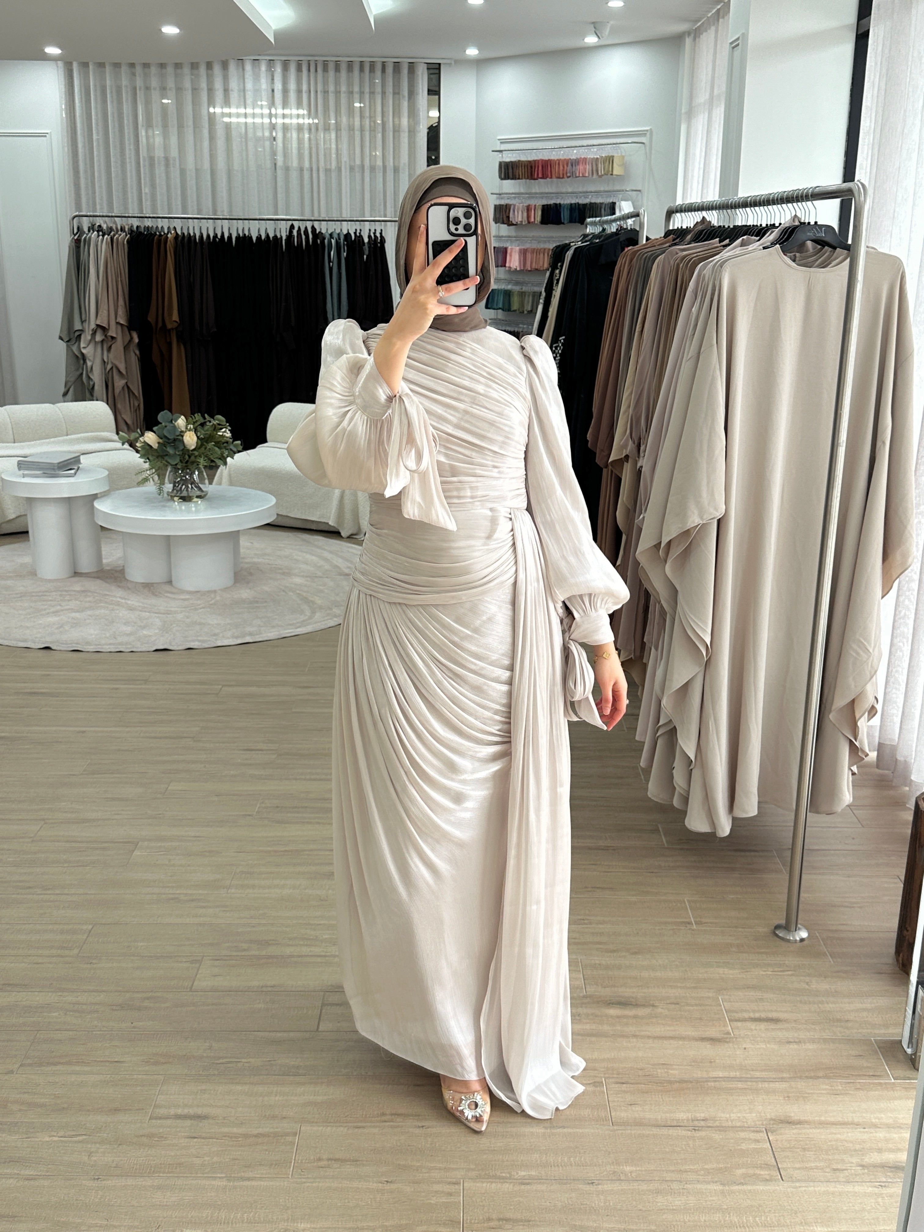 Model wearing the LAYAN Formal Dress, a floor-length gown in shiny organza fabric featuring all-over ruching, statement balloon sleeves with ribbon tie cuffs, a fitted waist with a drop panel, and a cascading skirt for an elegant, formal look.