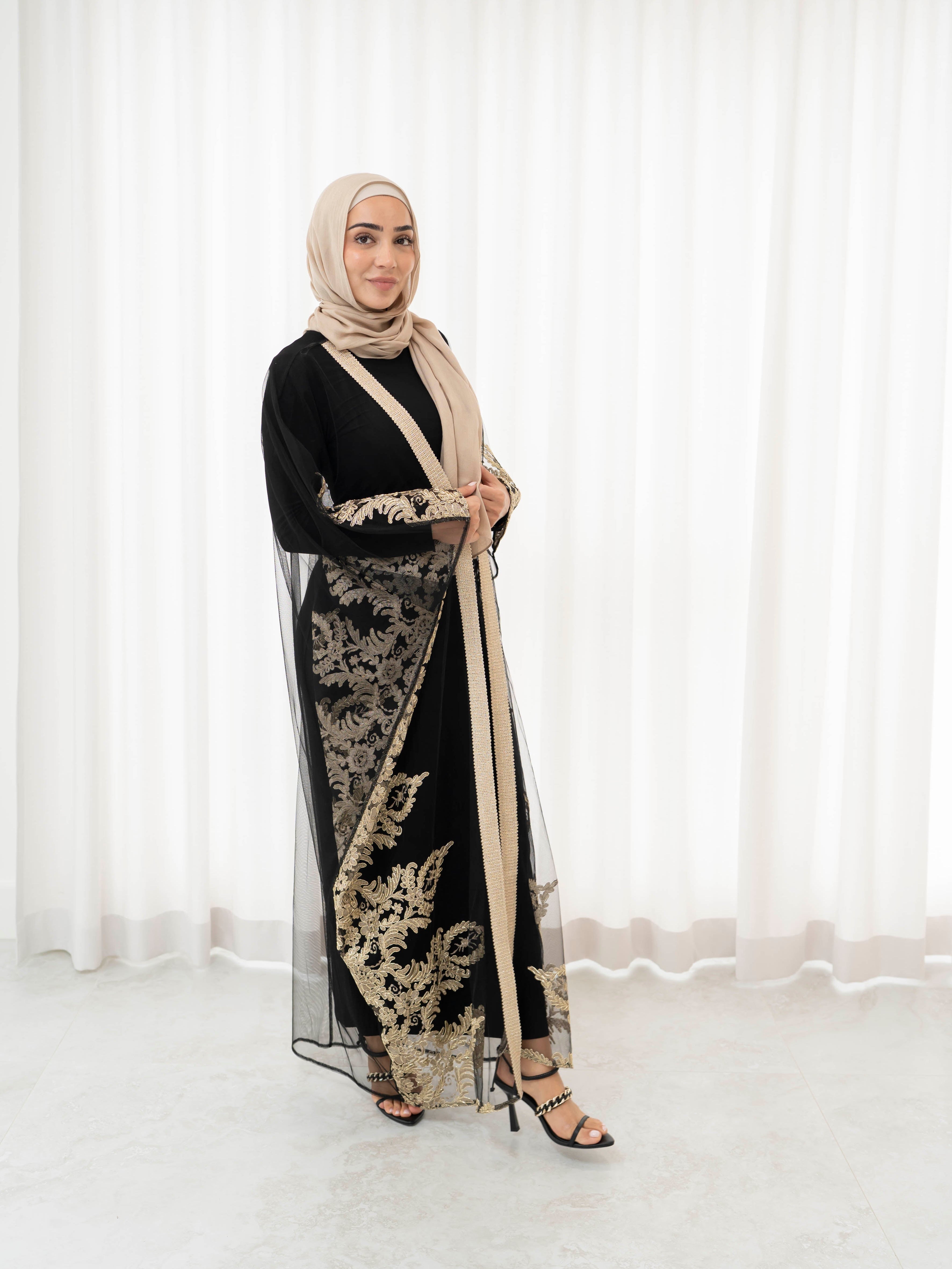 Elegant black lace abaya set with intricate gold embroidery woven throughout, creating a subtle regal shimmer. The outer layer features delicate lace detailing with refined gold accents that balance luxury and modesty. Paired with a coordinating long-sleeve black inner dress, the set offers full coverage and a smooth, flattering layered silhouette, designed for formal occasions and special events.