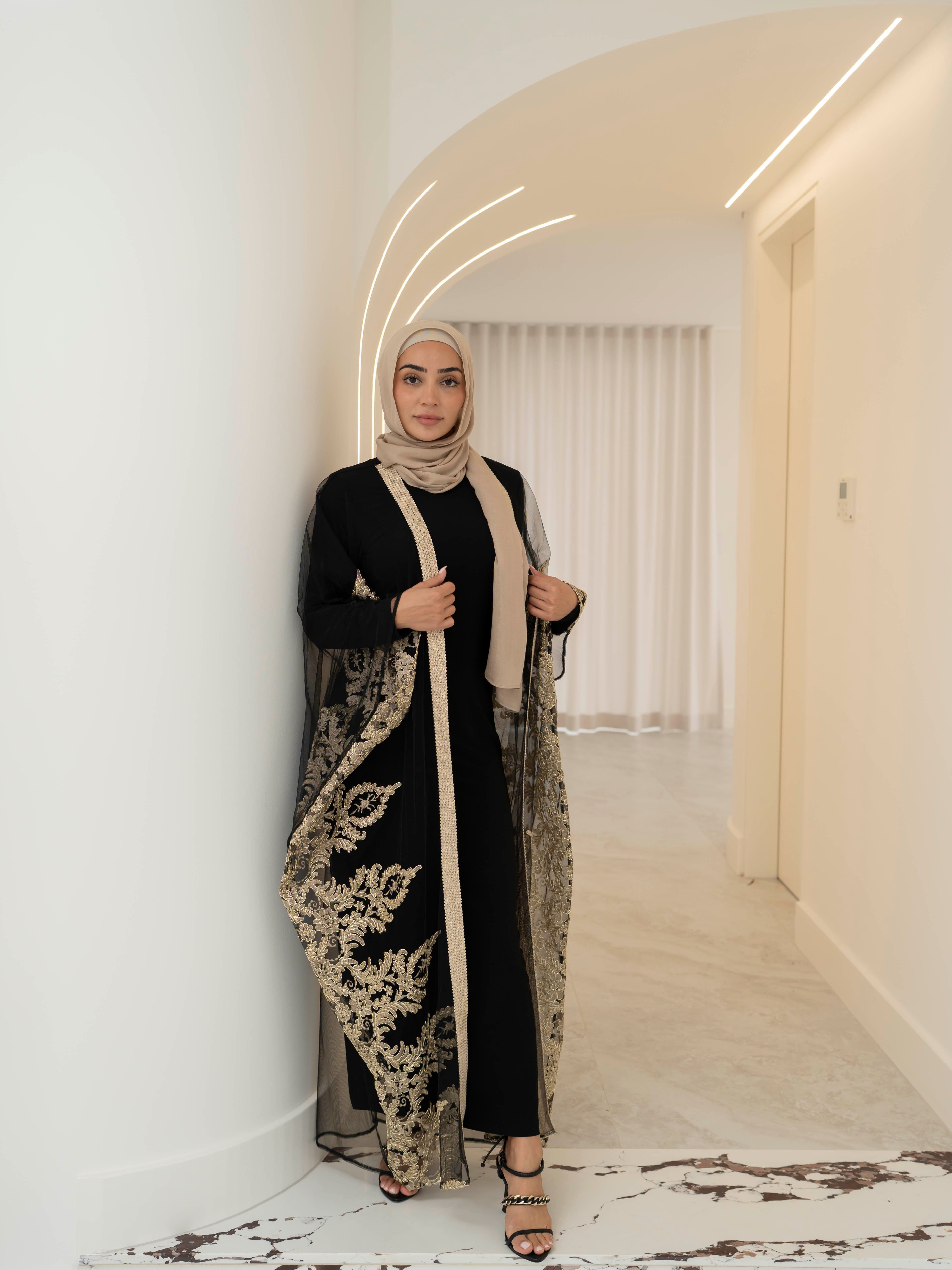 Elegant black lace abaya set with intricate gold embroidery woven throughout, creating a subtle regal shimmer. The outer layer features delicate lace detailing with refined gold accents that balance luxury and modesty. Paired with a coordinating long-sleeve black inner dress, the set offers full coverage and a smooth, flattering layered silhouette, designed for formal occasions and special events.