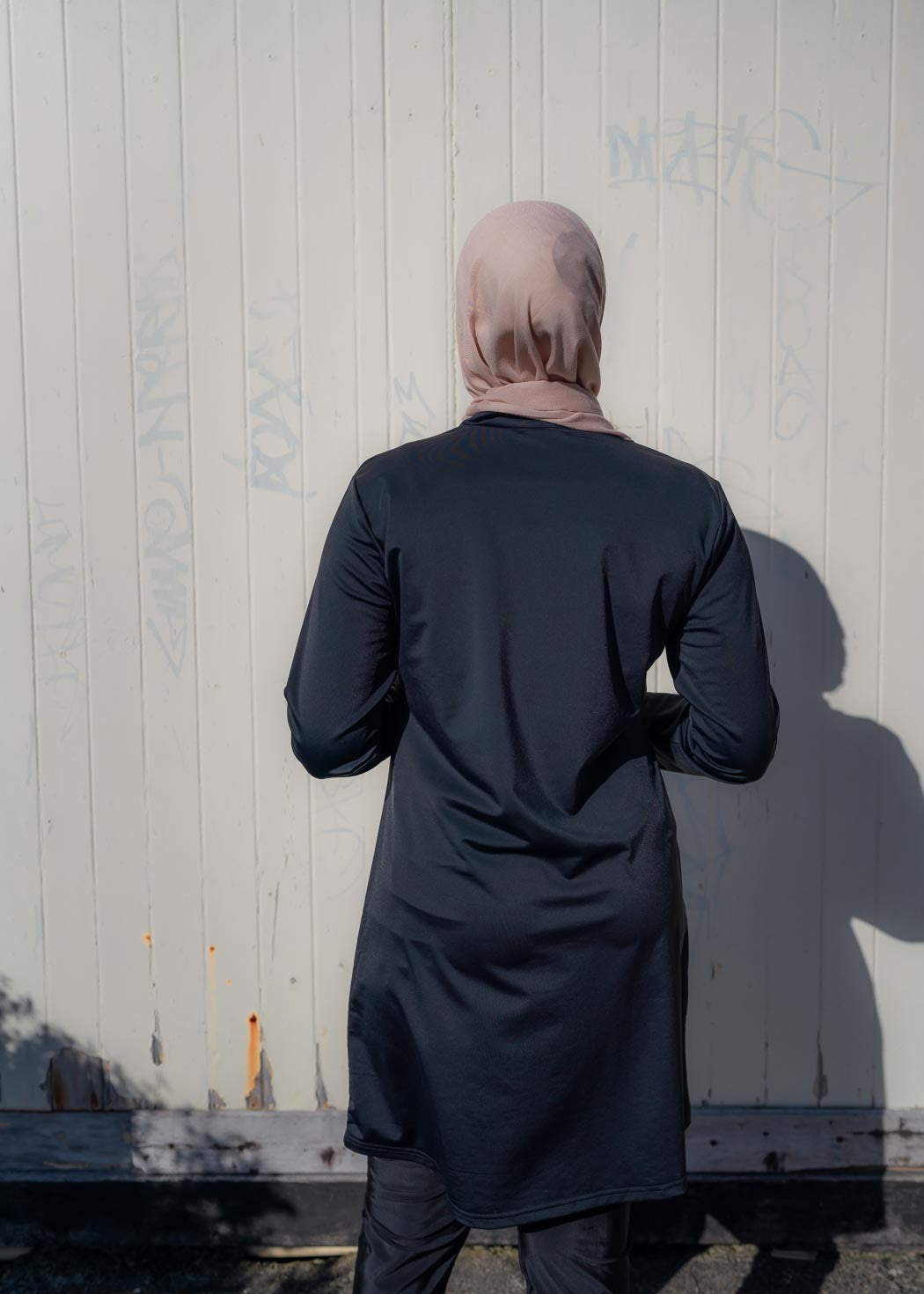 Model wearing the Marina modest swimwear set in black or mauve, featuring a long-sleeve top that falls above the knee and loose trousers with an elasticated waistband. Made from stretch scuba fabric (85% polyester, 15% elastane) for a comfortable fit.