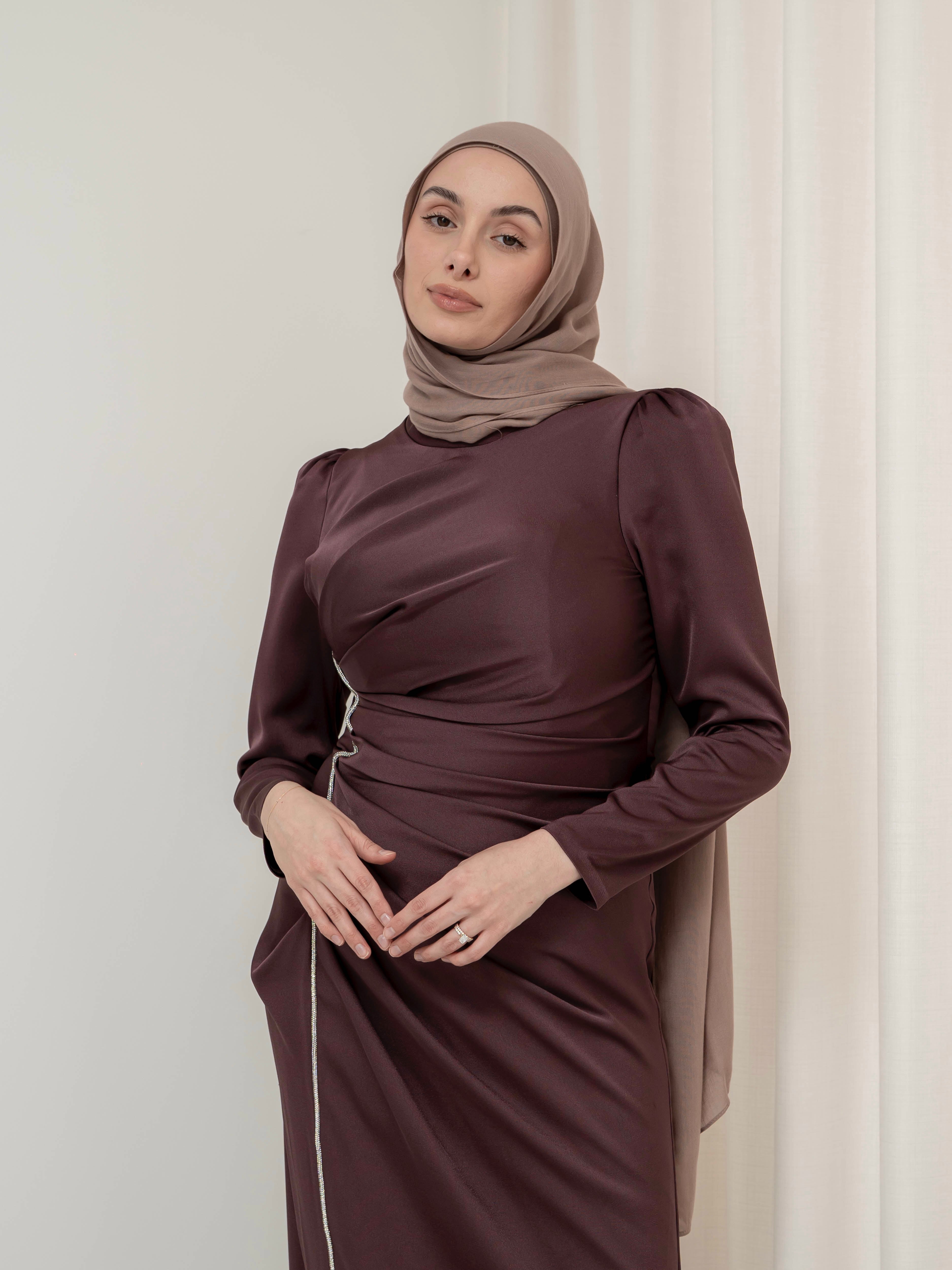 Elevate your formal look with the OLA FORMAL DRESS- MAHOGANY. Crafted from a shiny satin crepe fabric, this dress boasts elegant asymmetric gathers and a flattering silhouette that will make you stand out. Complete with long slim sleeves and a floor-skimming hem, this dress is perfect for any formal occasion.