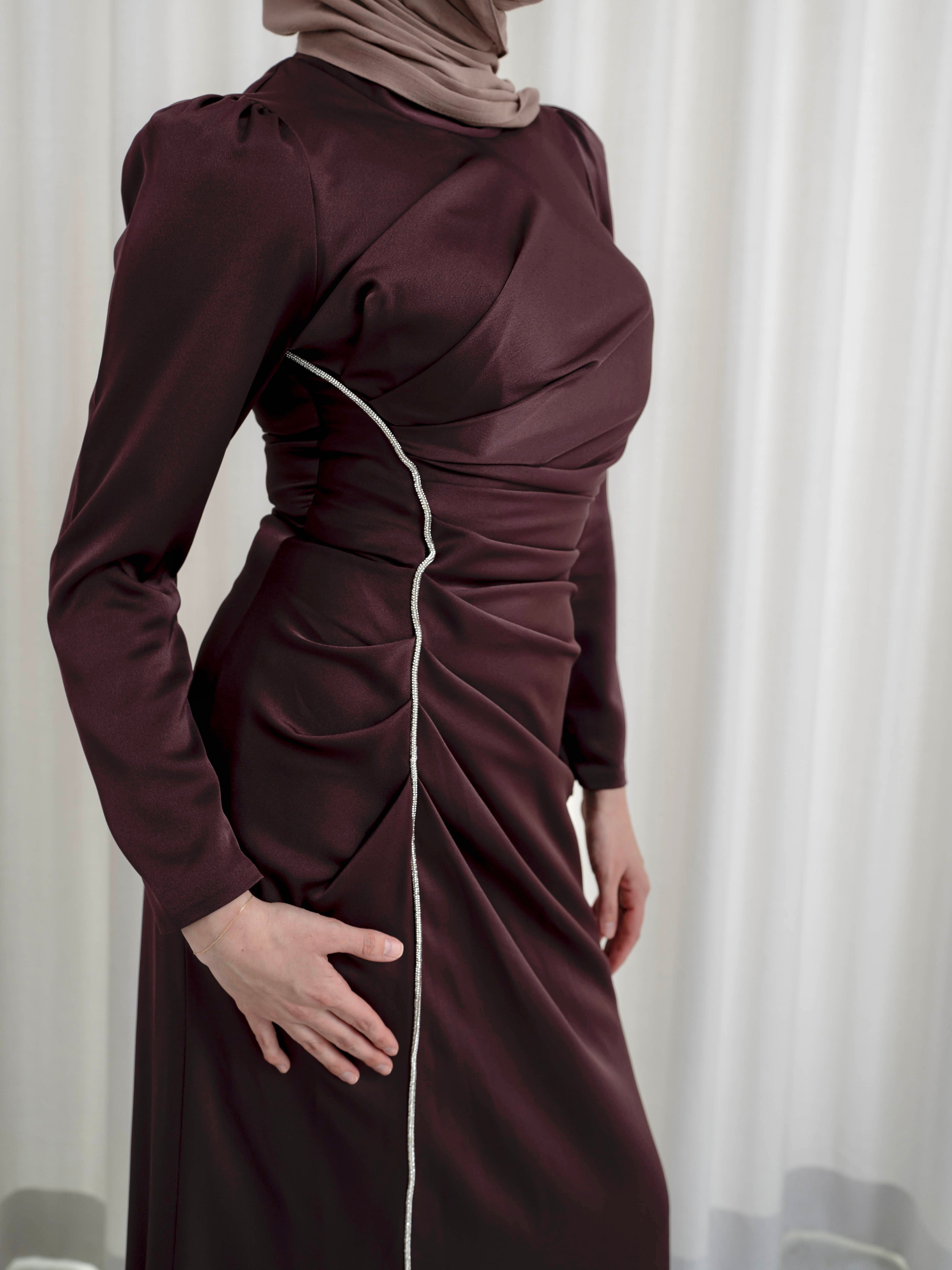 Elevate your formal look with the OLA FORMAL DRESS- MAHOGANY. Crafted from a shiny satin crepe fabric, this dress boasts elegant asymmetric gathers and a flattering silhouette that will make you stand out. Complete with long slim sleeves and a floor-skimming hem, this dress is perfect for any formal occasion.