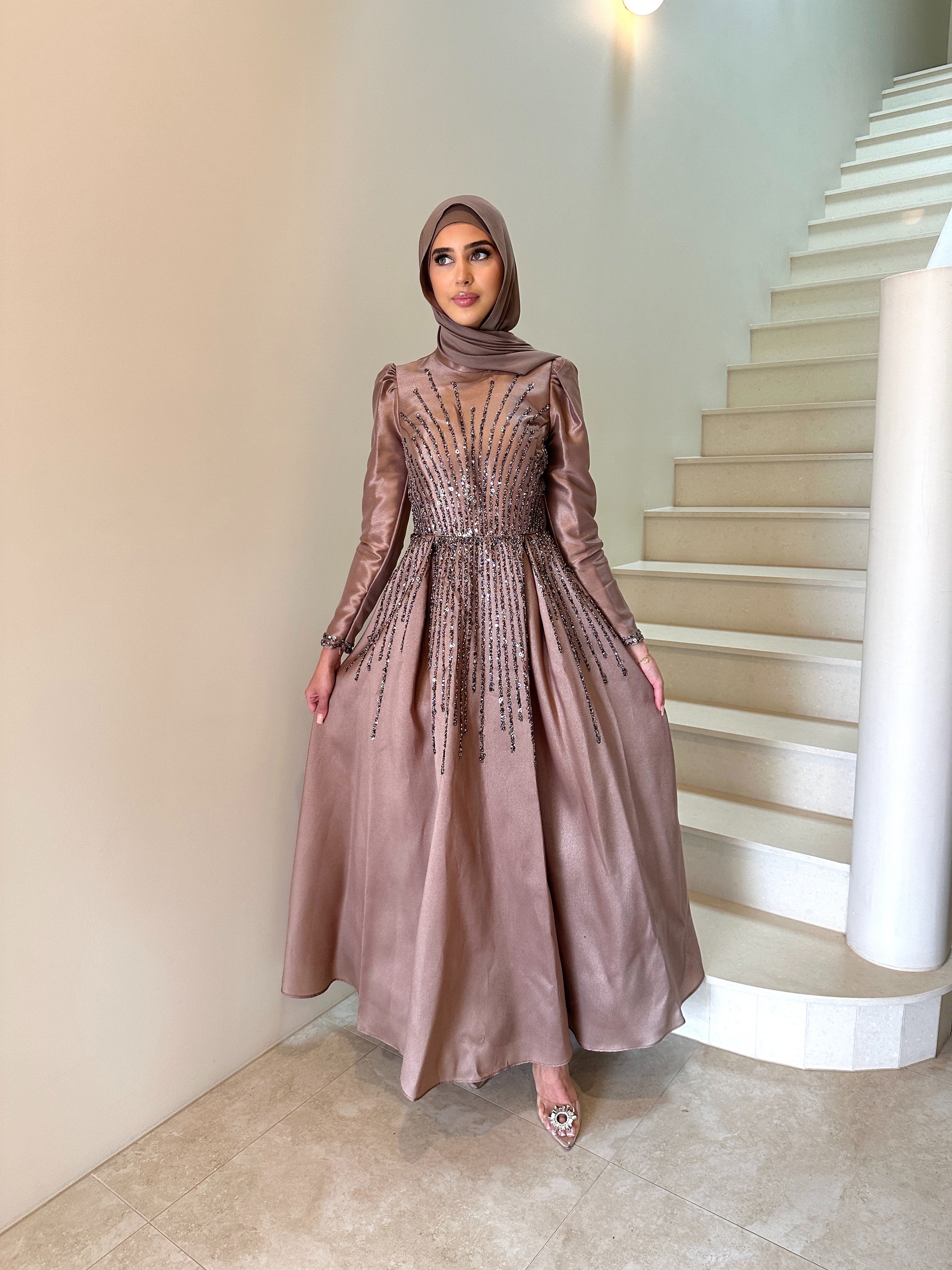 Shaima Formal Dress in shiny satin with a fitted waist and ball gown skirt. Features high neck, puffy shoulders, long sleeves, and sequined embellishments on bodice and skirt with an invisible back zip — perfect for formal occasions.