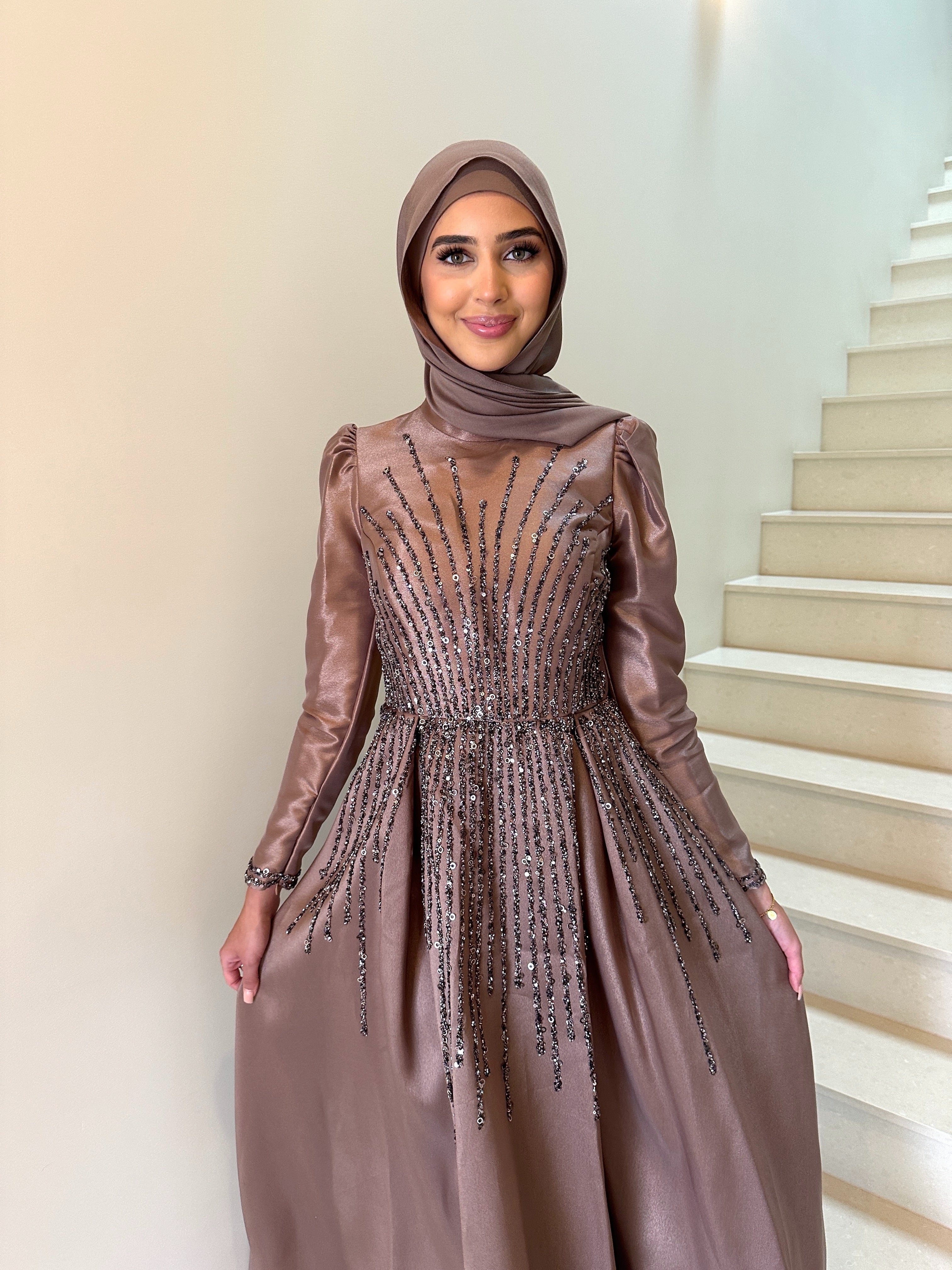 Shaima Formal Dress in shiny satin with a fitted waist and ball gown skirt. Features high neck, puffy shoulders, long sleeves, and sequined embellishments on bodice and skirt with an invisible back zip — perfect for formal occasions.