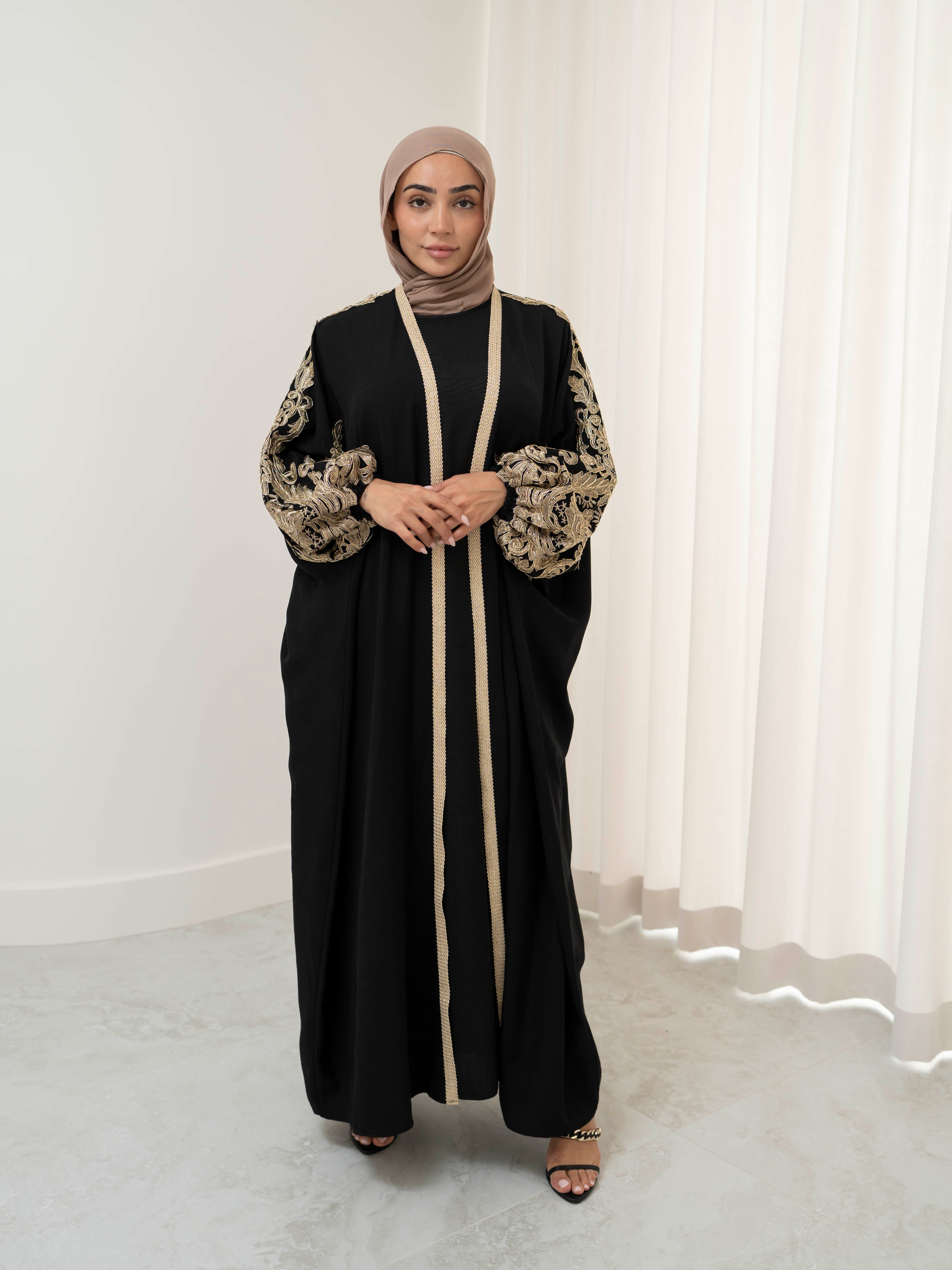 Model wearing the Haya two-piece abaya set featuring a gold-embroidered open abaya layered over an inner dress, styled for a modest and elegant look suitable for Ramadan and Eid.