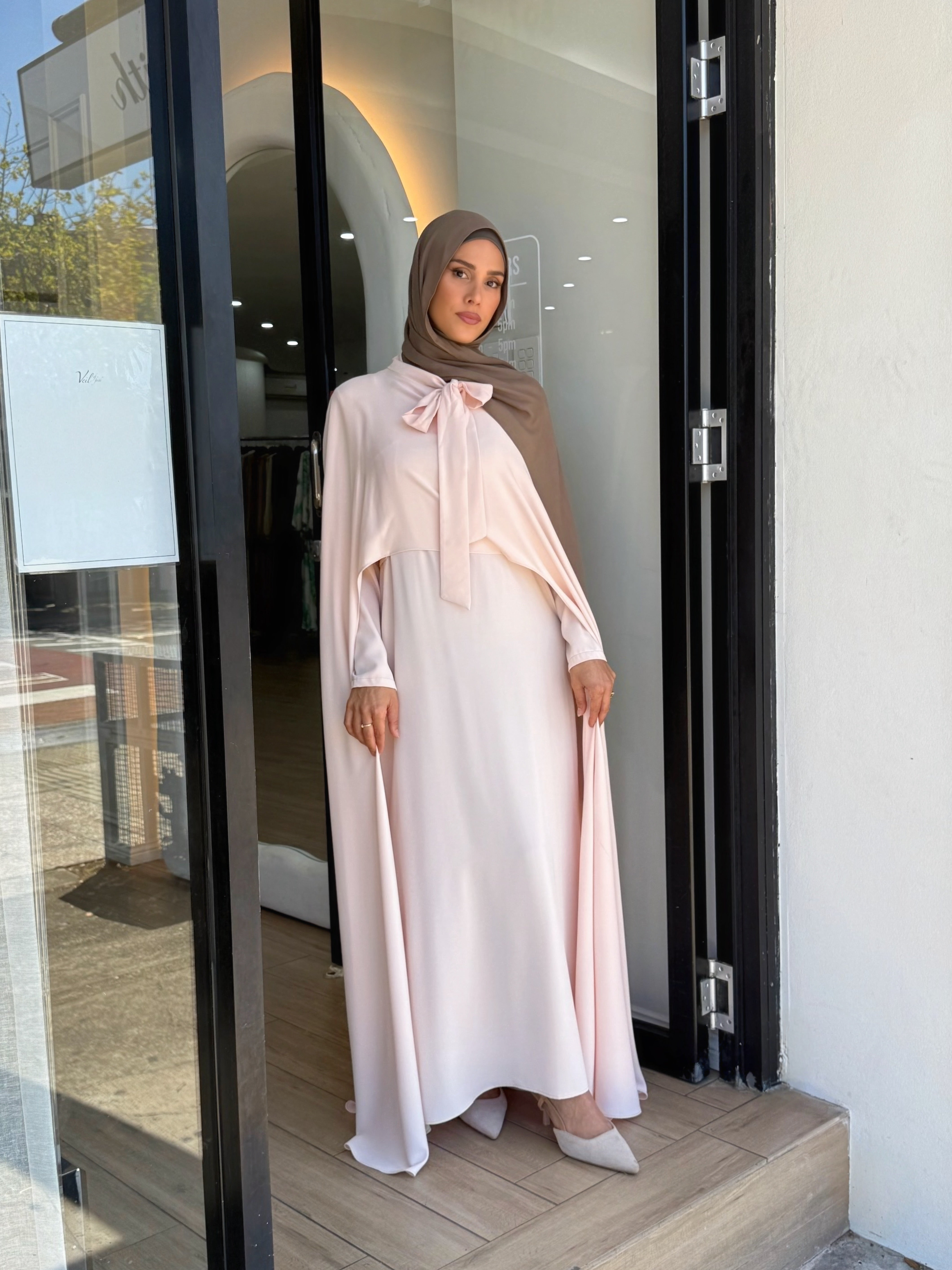 Grace meets fluidity in this captivating cape dress. Designed with a soft bow-tie neckline and a flowing overlay that drapes effortlessly over the shoulders, this piece radiates femininity and poise. These soft colours complement all skin tones, while the lightweight satin finish brings an understated elegance perfect for formal evenings and events.