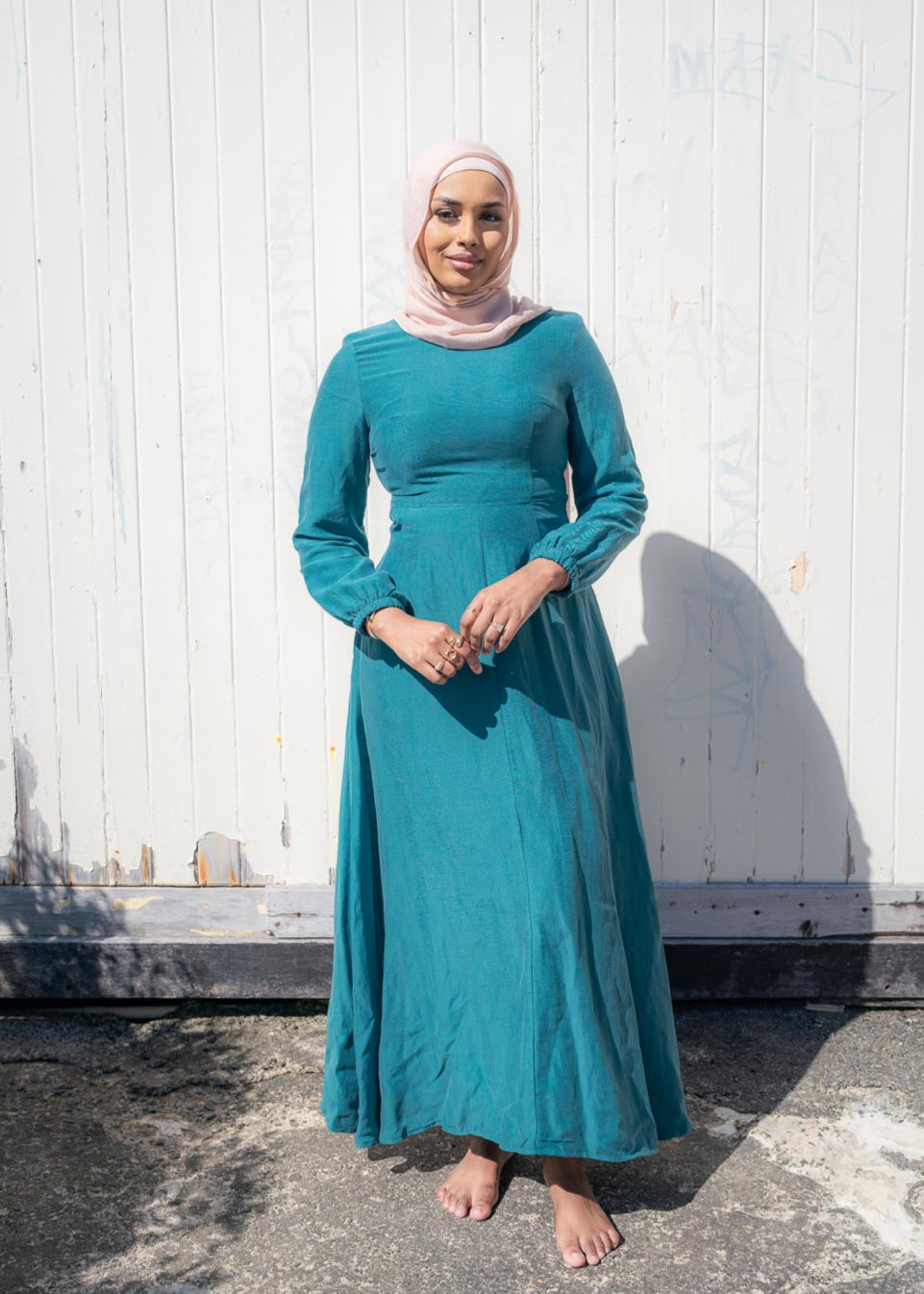 Amira Linen Dress in a soft linen-blend fabric with long sleeves and a fitted bodice featuring limited stretch. Designed with an empire waist that flows into a loose high-low skirt for an elegant, flattering silhouette suitable for special occasions.