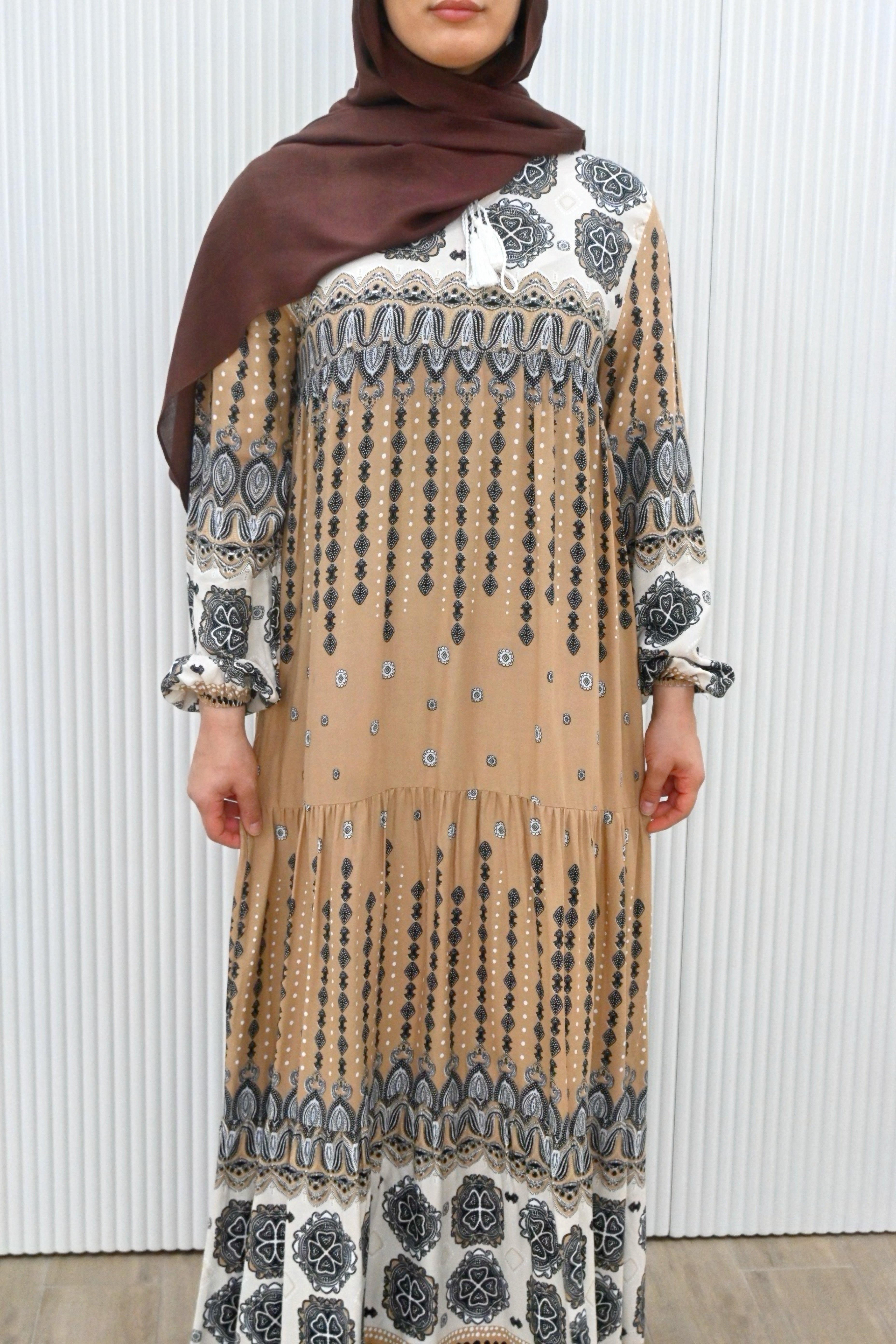 This is a long, loose-fit maxi dress with long sleeves. It features floral and geometric patterns with a flowy gathered design, making it stylish and modest.