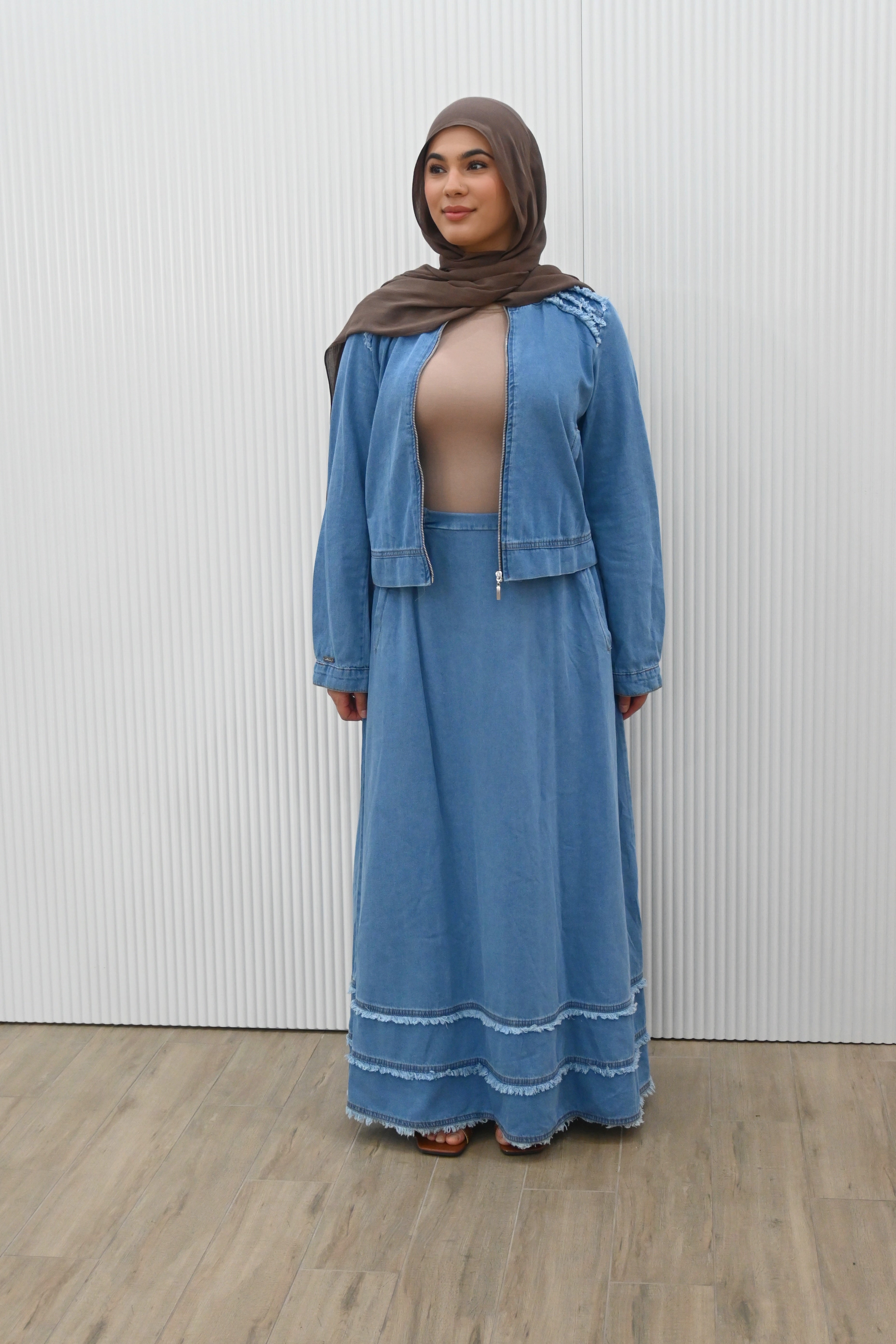 This is a two-piece modest denim-style outfit featuring a long A-line skirt and a matching zip-up jacket. The skirt has layered frayed hem details for a casual chic look, while the jacket is designed with full sleeves and light embroidery accents on the shoulder. Paired with a plain inner top, this set combines comfort and style, making it perfect for everyday wear or casual outings.