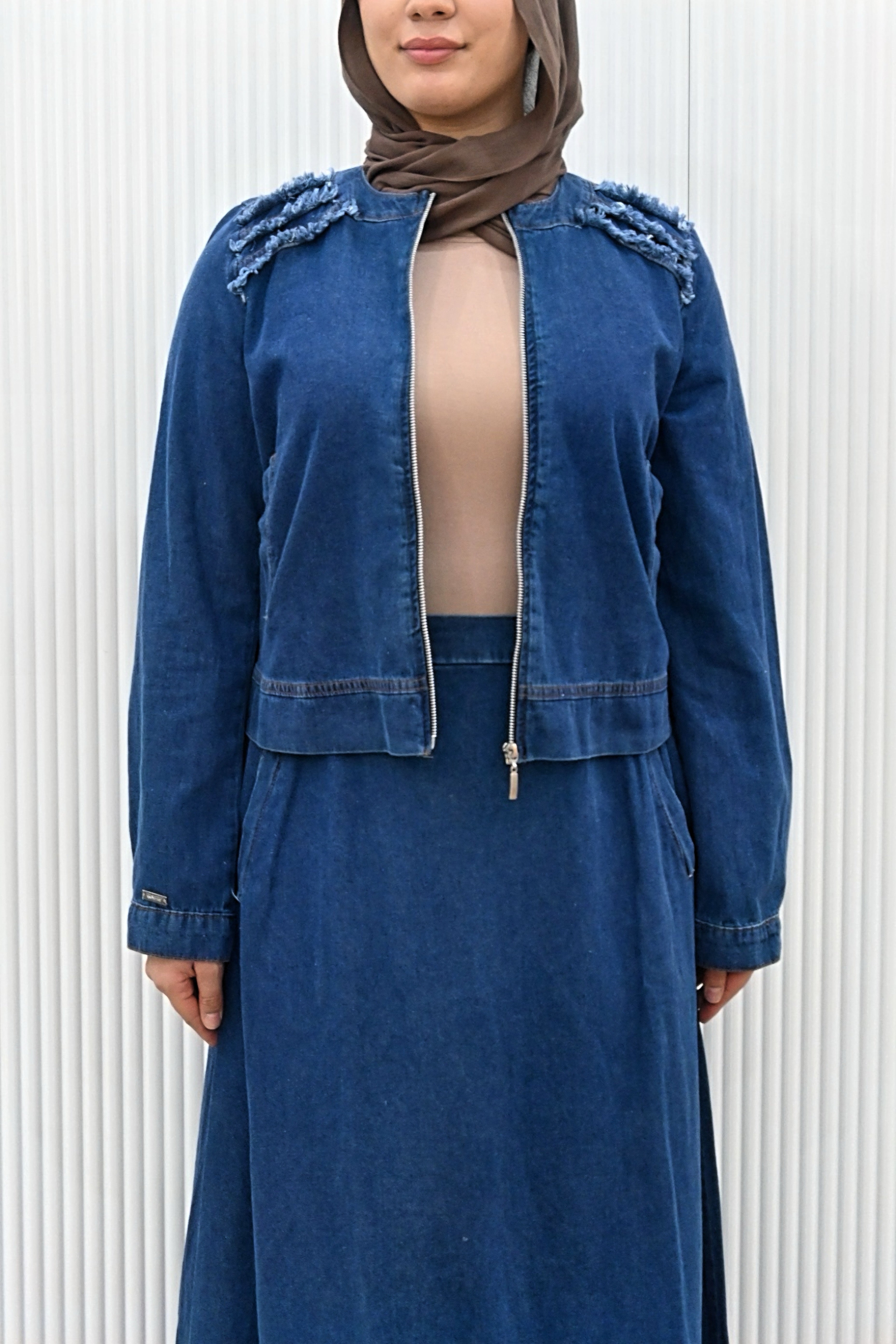 This is a two-piece modest denim-style outfit featuring a long A-line skirt and a matching zip-up jacket. The skirt has layered frayed hem details for a casual chic look, while the jacket is designed with full sleeves and light embroidery accents on the shoulder. Paired with a plain inner top, this set combines comfort and style, making it perfect for everyday wear or casual outings.