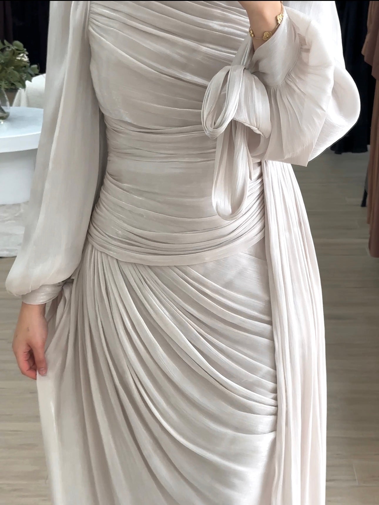 Model wearing the LAYAN Formal Dress, a floor-length gown in shiny organza fabric featuring all-over ruching, statement balloon sleeves with ribbon tie cuffs, a fitted waist with a drop panel, and a cascading skirt for an elegant, formal look.