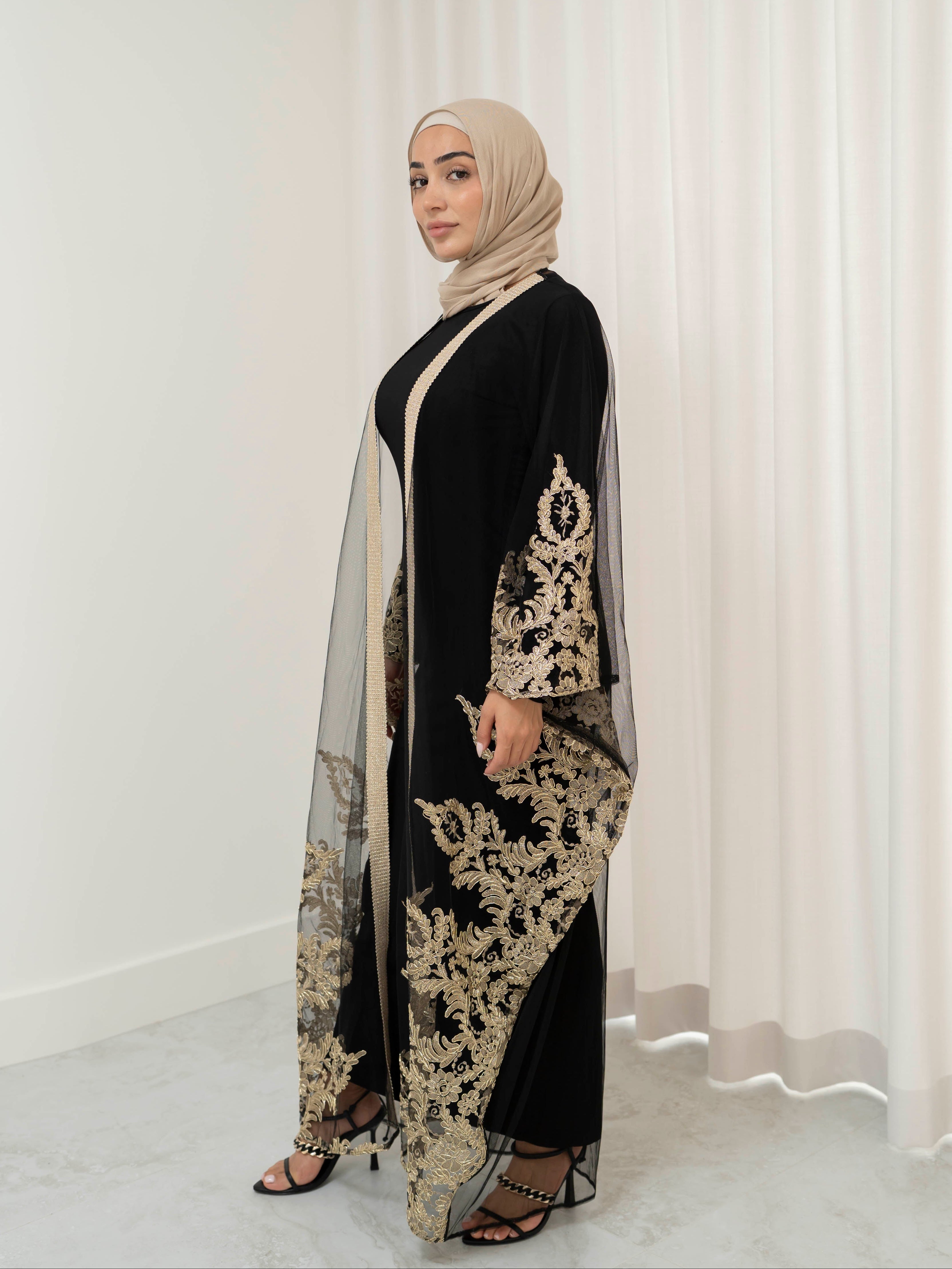 Elegant black lace abaya set with intricate gold embroidery woven throughout, creating a subtle regal shimmer. The outer layer features delicate lace detailing with refined gold accents that balance luxury and modesty. Paired with a coordinating long-sleeve black inner dress, the set offers full coverage and a smooth, flattering layered silhouette, designed for formal occasions and special events.