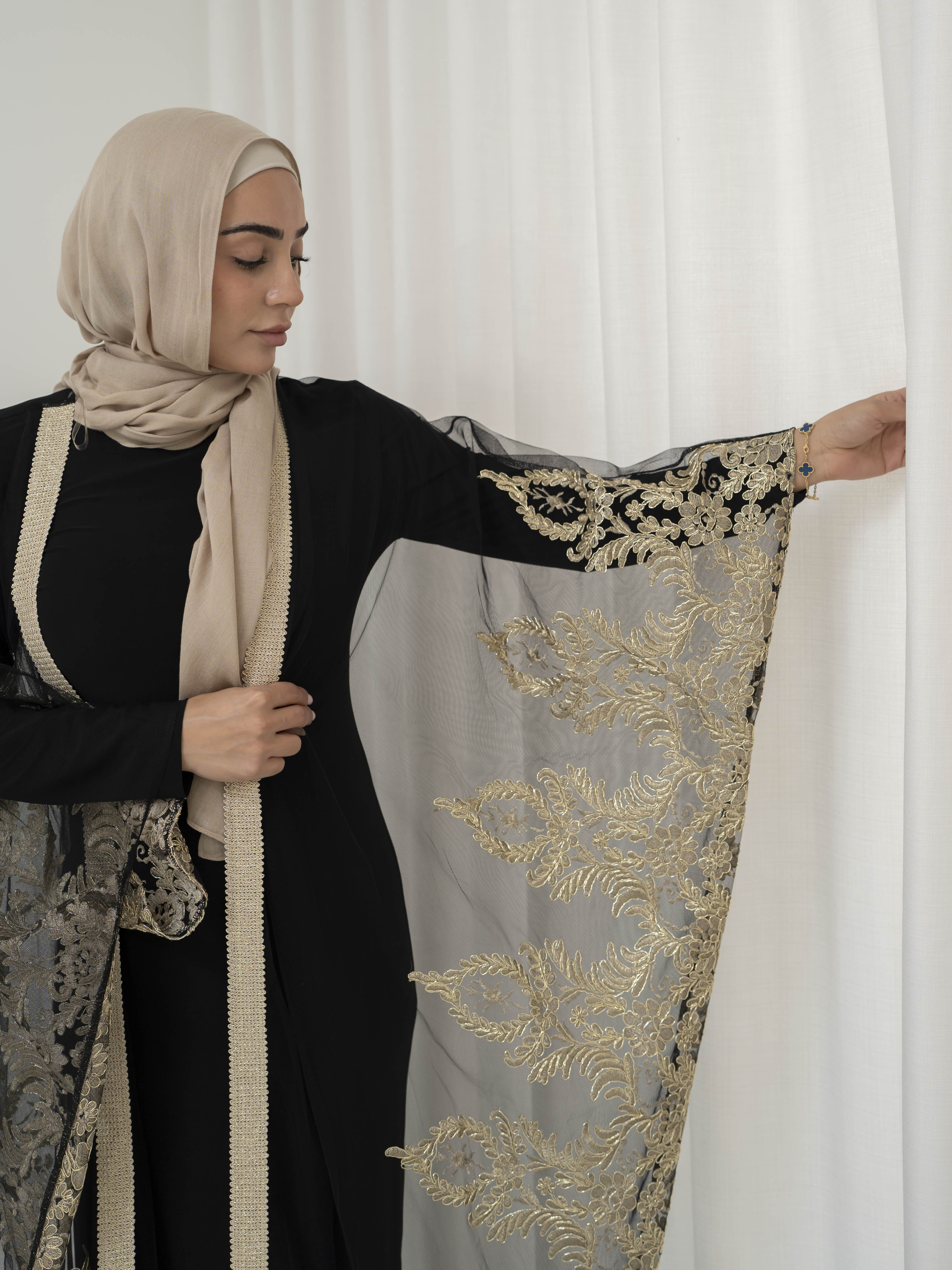 Elegant black lace abaya set with intricate gold embroidery woven throughout, creating a subtle regal shimmer. The outer layer features delicate lace detailing with refined gold accents that balance luxury and modesty. Paired with a coordinating long-sleeve black inner dress, the set offers full coverage and a smooth, flattering layered silhouette, designed for formal occasions and special events.
