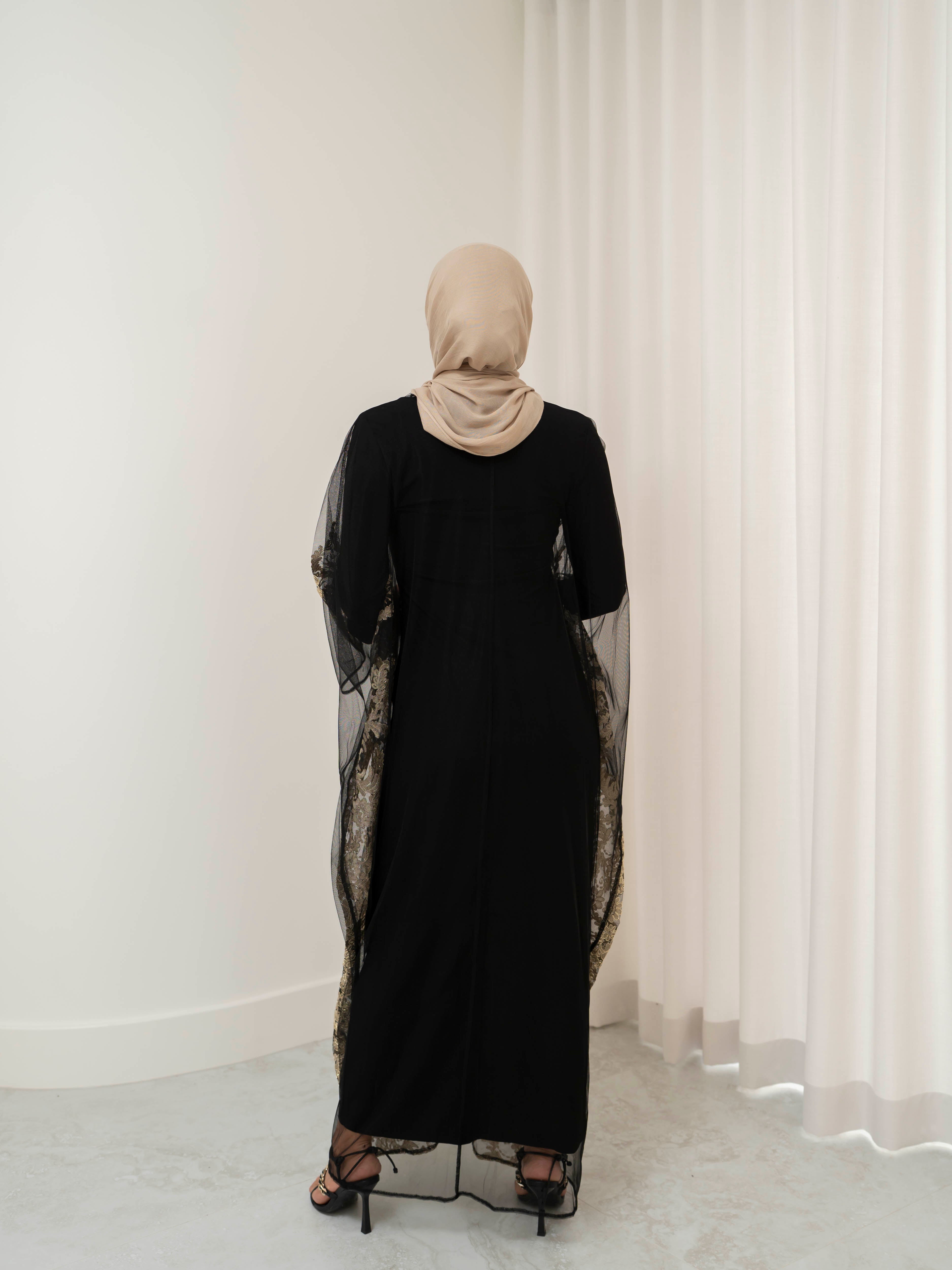 Elegant black lace abaya set with intricate gold embroidery woven throughout, creating a subtle regal shimmer. The outer layer features delicate lace detailing with refined gold accents that balance luxury and modesty. Paired with a coordinating long-sleeve black inner dress, the set offers full coverage and a smooth, flattering layered silhouette, designed for formal occasions and special events.