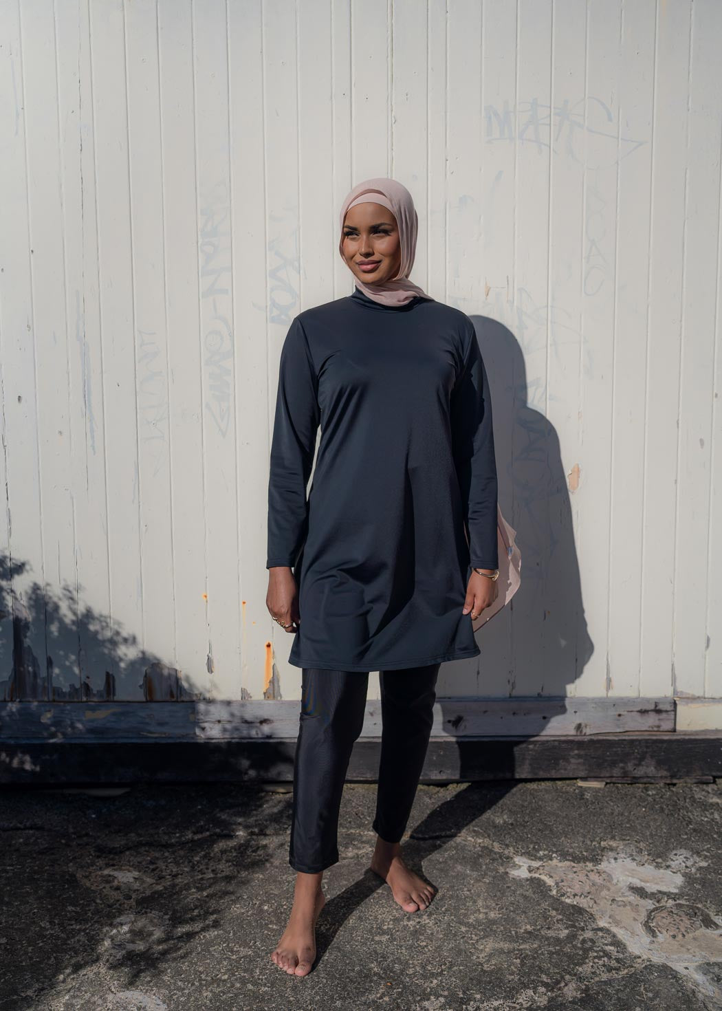 Model wearing the Marina modest swimwear set in black or mauve, featuring a long-sleeve top that falls above the knee and loose trousers with an elasticated waistband. Made from stretch scuba fabric (85% polyester, 15% elastane) for a comfortable fit.