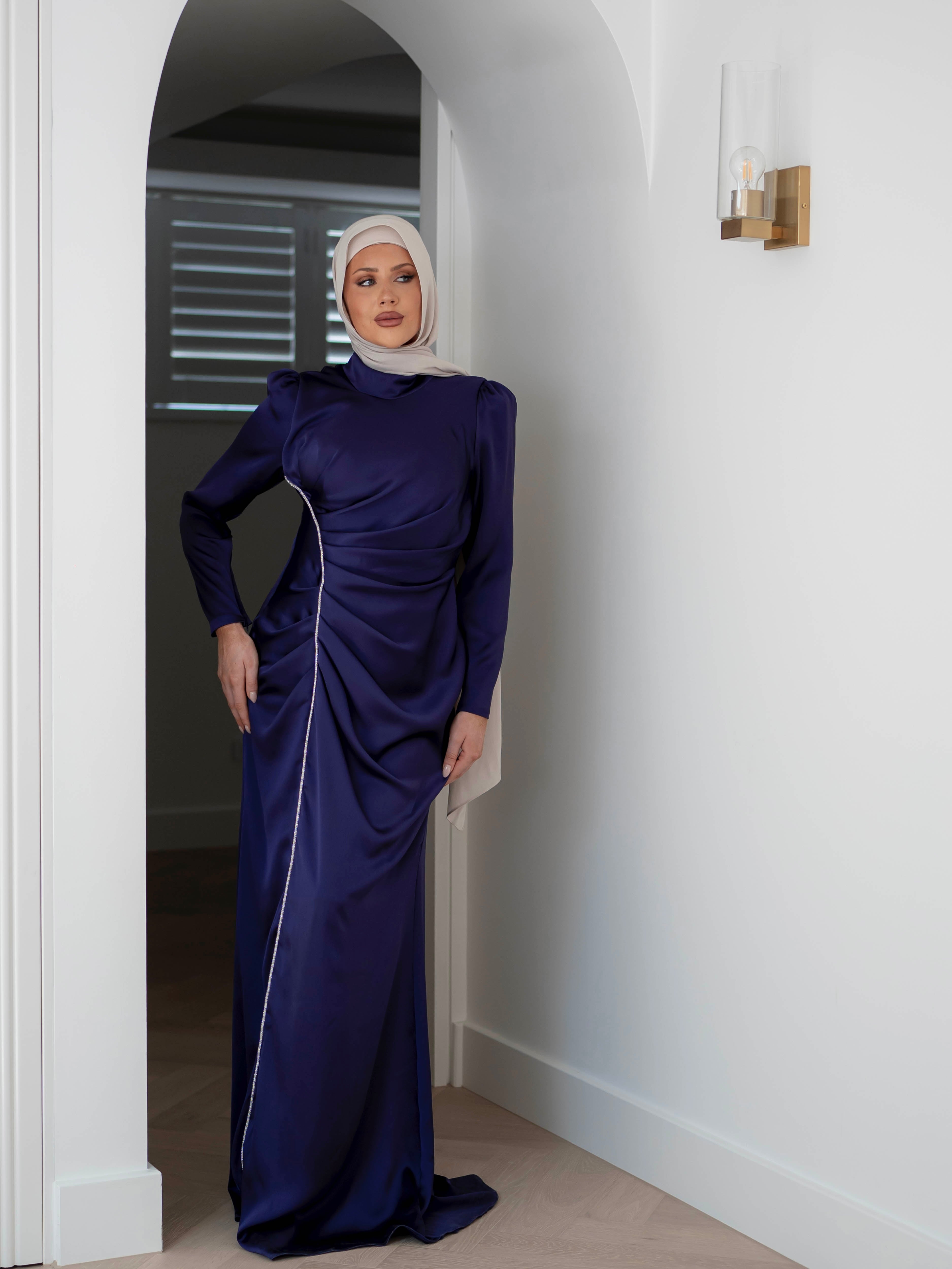 Elevate your formal look with the OLA FORMAL DRESS- INDIGO. Crafted from a shiny satin crepe fabric, this dress boasts elegant asymmetric gathers and a flattering silhouette that will make you stand out. Complete with long slim sleeves and a floor-skimming hem, this dress is perfect for any formal occasion.