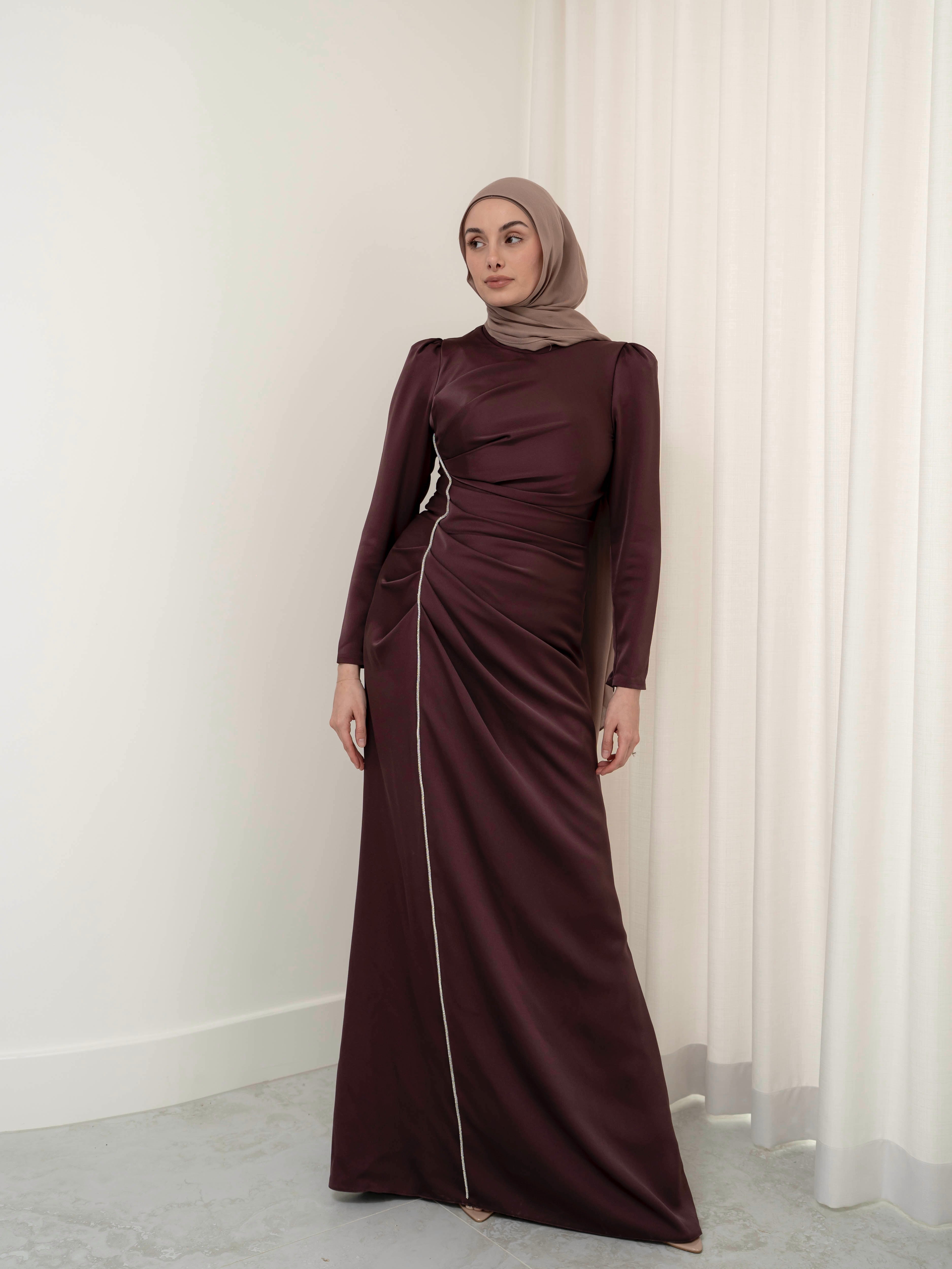 Elevate your formal look with the OLA FORMAL DRESS- MAHOGANY. Crafted from a shiny satin crepe fabric, this dress boasts elegant asymmetric gathers and a flattering silhouette that will make you stand out. Complete with long slim sleeves and a floor-skimming hem, this dress is perfect for any formal occasion.