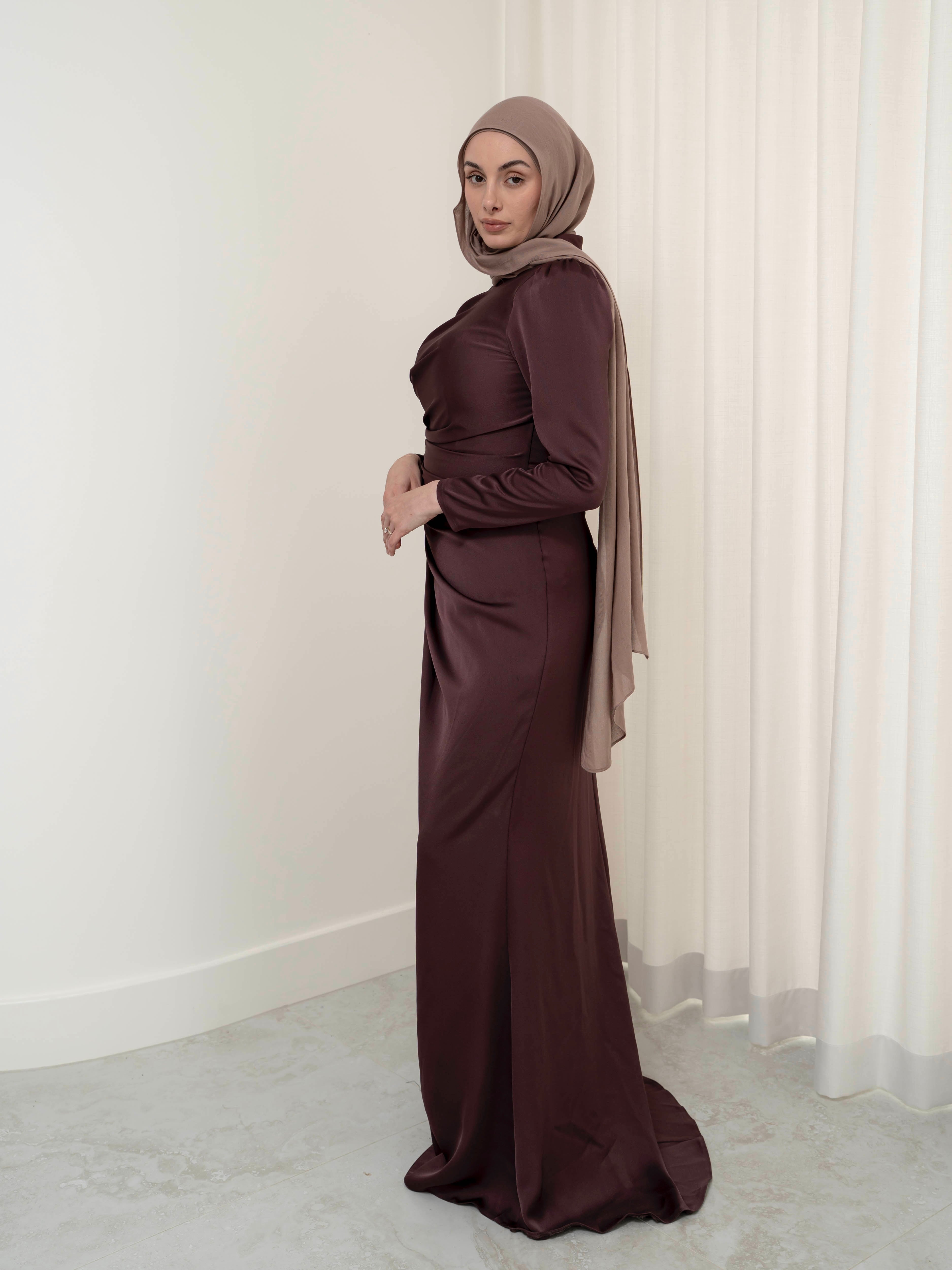 Elevate your formal look with the OLA FORMAL DRESS- MAHOGANY. Crafted from a shiny satin crepe fabric, this dress boasts elegant asymmetric gathers and a flattering silhouette that will make you stand out. Complete with long slim sleeves and a floor-skimming hem, this dress is perfect for any formal occasion.