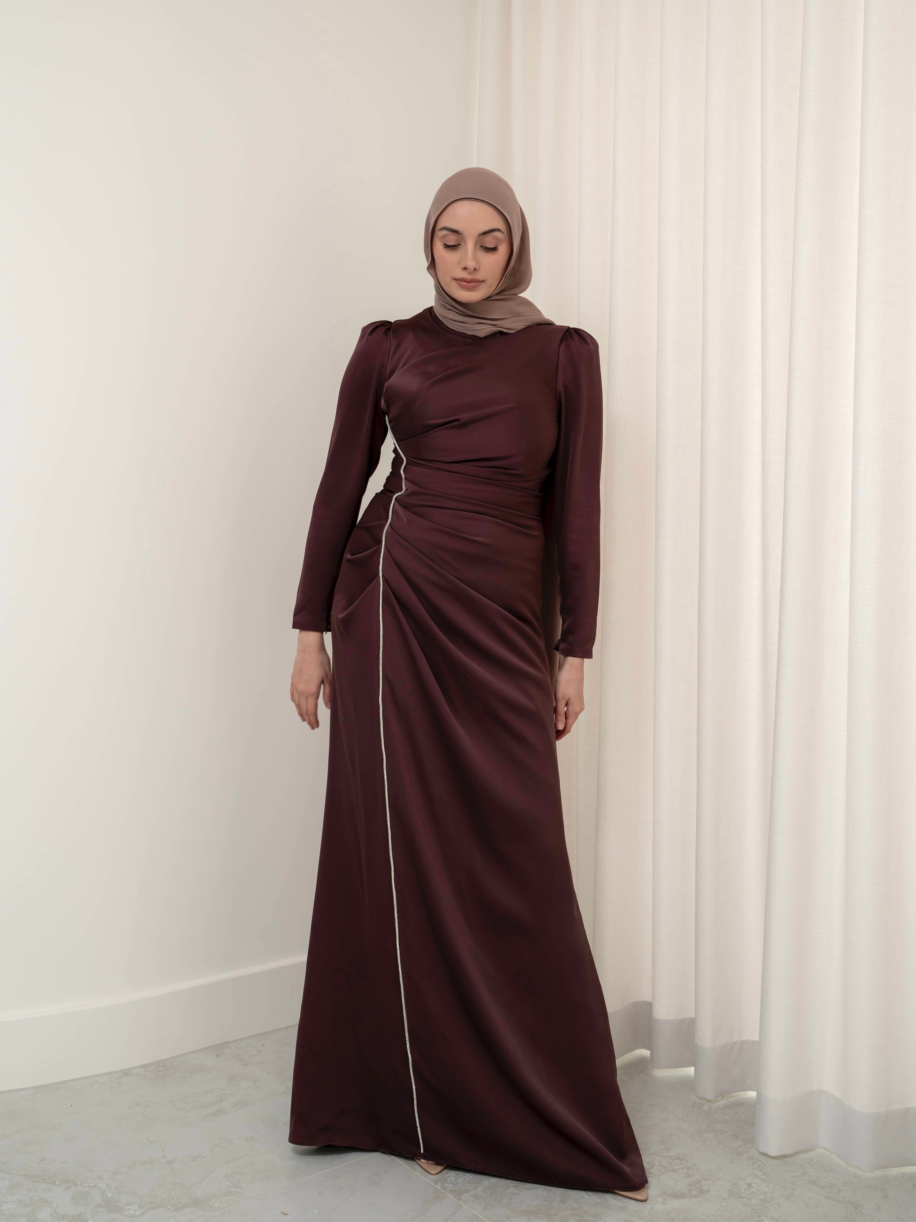 Elevate your formal look with the OLA FORMAL DRESS- MAHOGANY. Crafted from a shiny satin crepe fabric, this dress boasts elegant asymmetric gathers and a flattering silhouette that will make you stand out. Complete with long slim sleeves and a floor-skimming hem, this dress is perfect for any formal occasion.