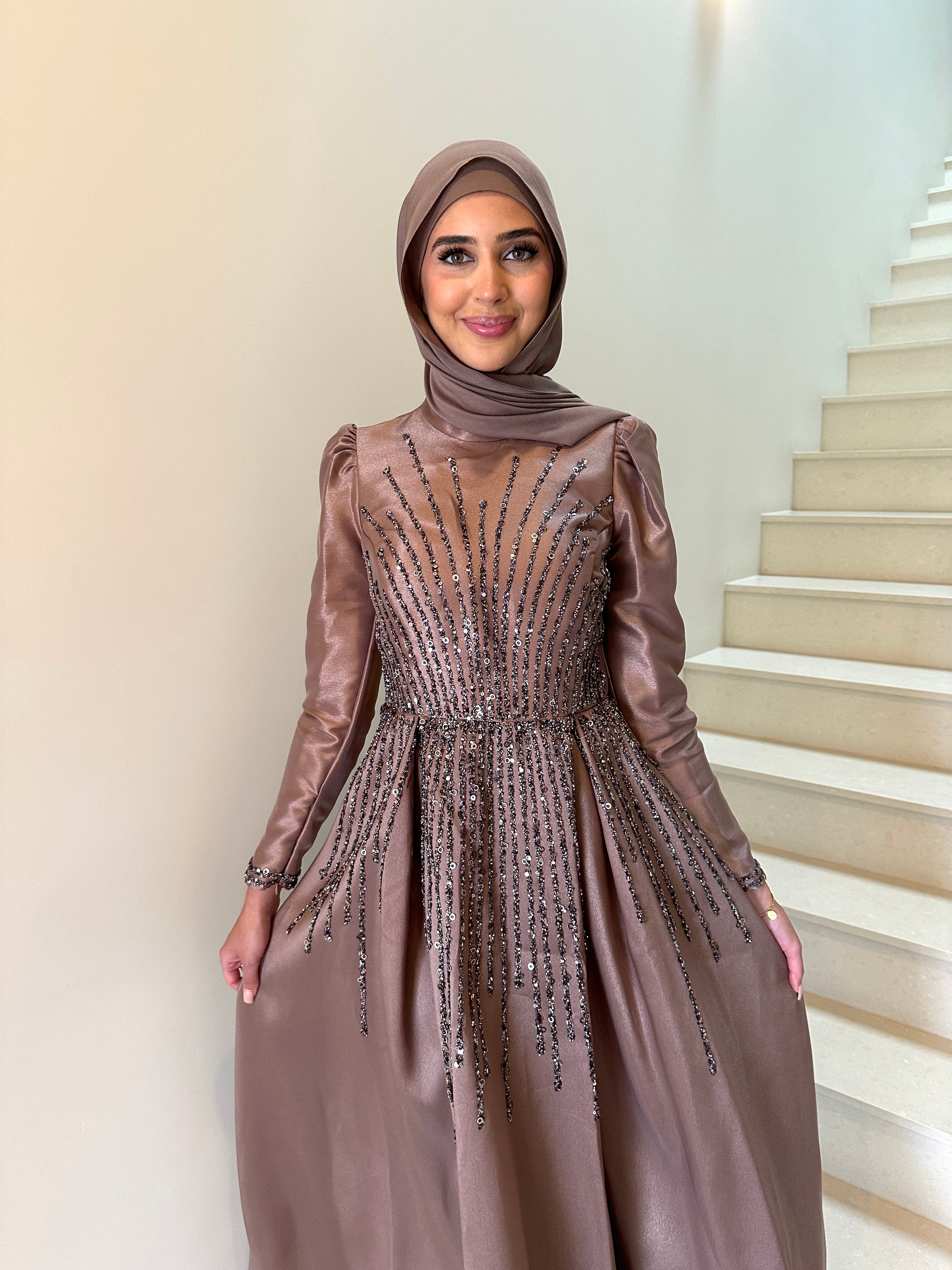 Shaima Formal Dress in shiny satin with a fitted waist and ball gown skirt. Features high neck, puffy shoulders, long sleeves, and sequined embellishments on bodice and skirt with an invisible back zip — perfect for formal occasions.