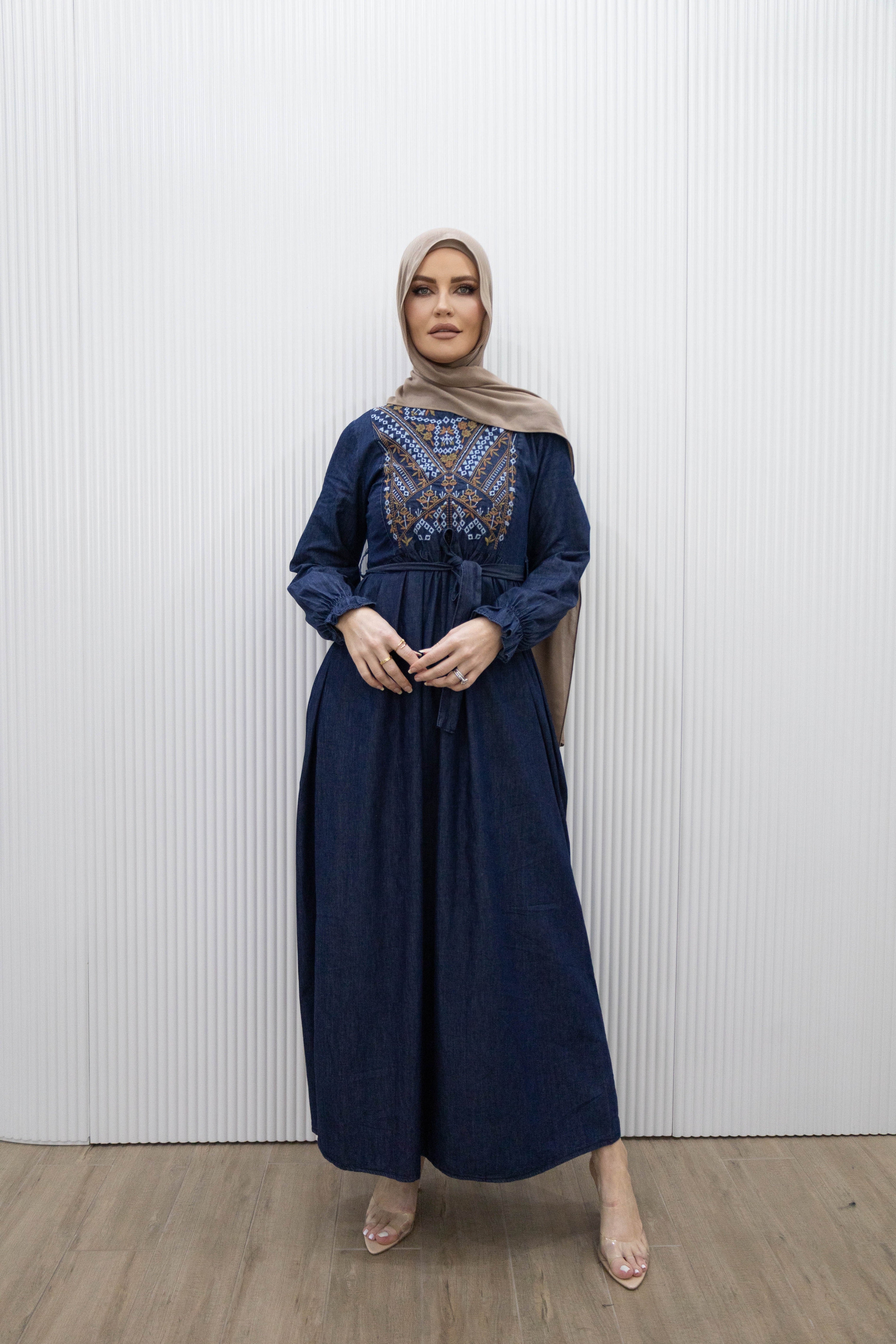 Taseem Dress in lightweight denim-style fabric with embroidered paisley design, long frill-cuffed sleeves, waist tie, and flared maxi skirt for a flattering, elegant silhouette.